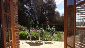 A patio with two chairs and a table, a stone wall, and a view of a garden with trees and plants. - Wagners Cottages (Swansea)