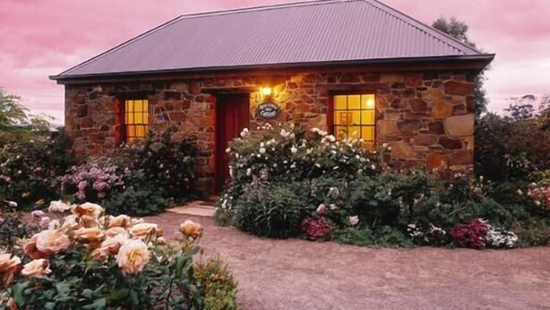 A stone house with a red door and windows, surrounded by a garden with various flowers and plants. - Wagners Cottages (Swansea)