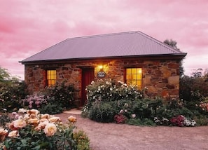 Una casa de piedra con puerta y ventanas rojas, rodeada de un jardín con diversas flores y plantas.
