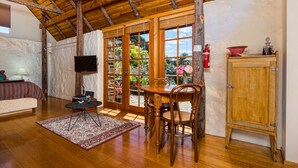 A cozy room with a wooden ceiling, a dining table with chairs, a television, and a cabinet. - Wagners Cottages (Swansea)