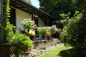 A garden with a variety of plants and flowers, a wooden pergola, and a building with a sloped roof.