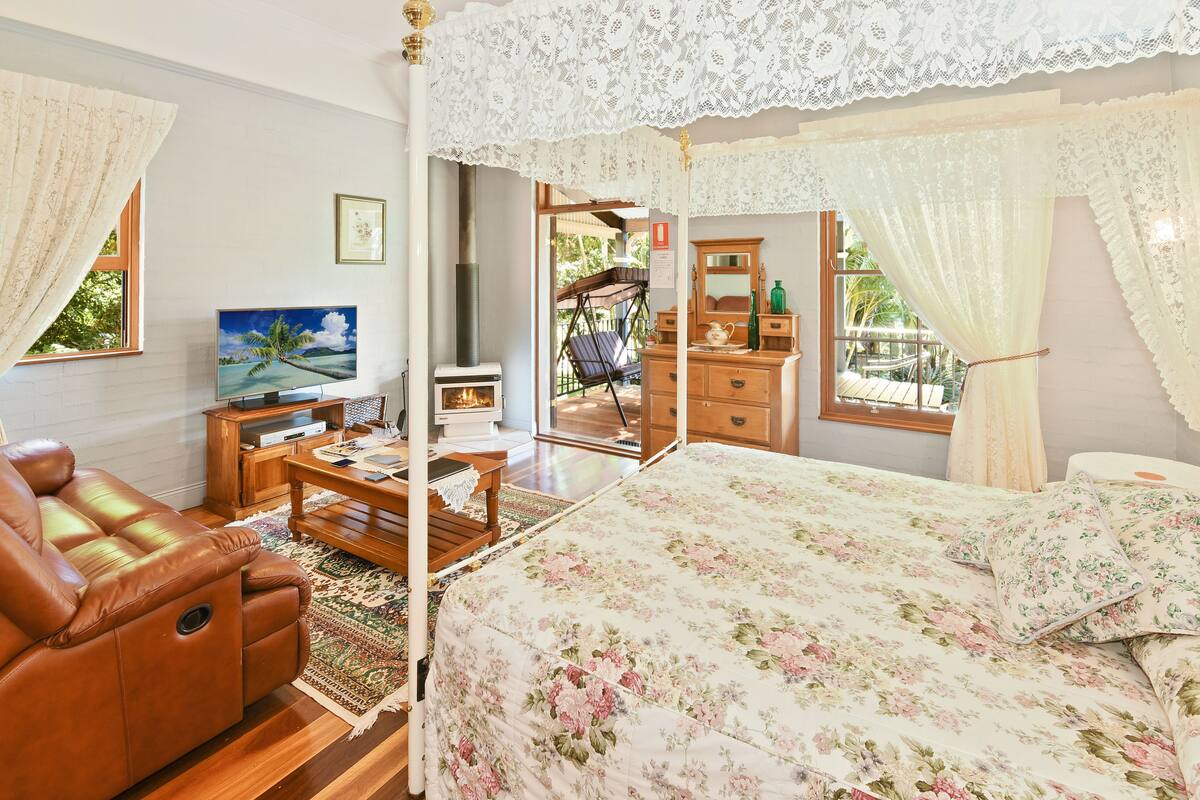 Ein Schlafzimmer mit einem Himmelbett, einem Ledersofa, einem Fernseher und einem Kamin.