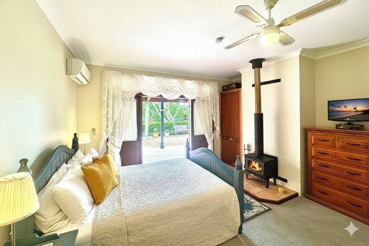 Ein Schlafzimmer mit Bett, Deckenventilator, Kamin, Fernseher und Blick ins Freie.
