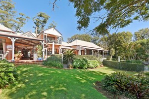 A two-story house with a covered porch, a well-maintained lawn, and various plants.