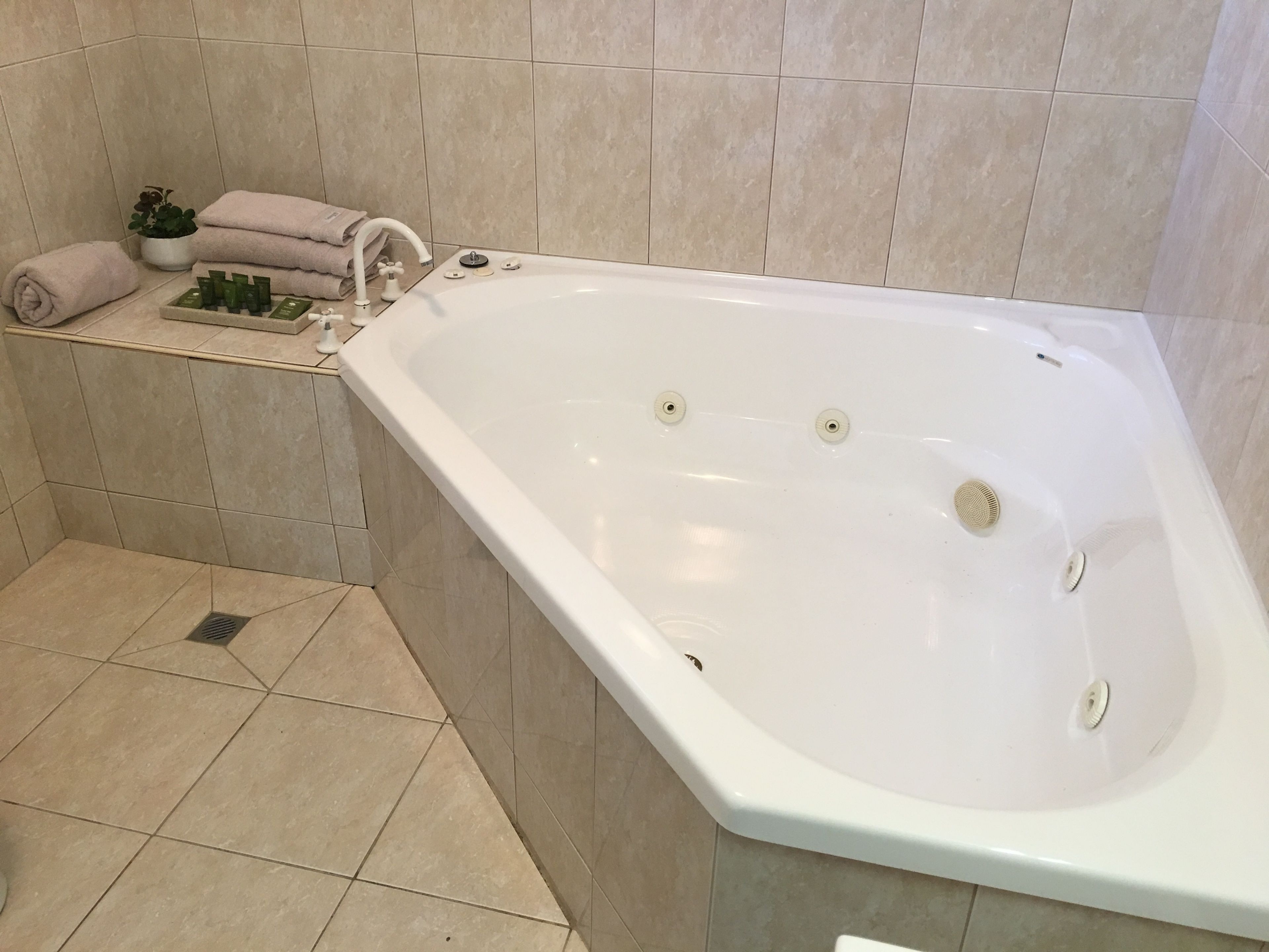 A modern bathroom with a large bathtub, a small sink, and a shelf with toiletries.