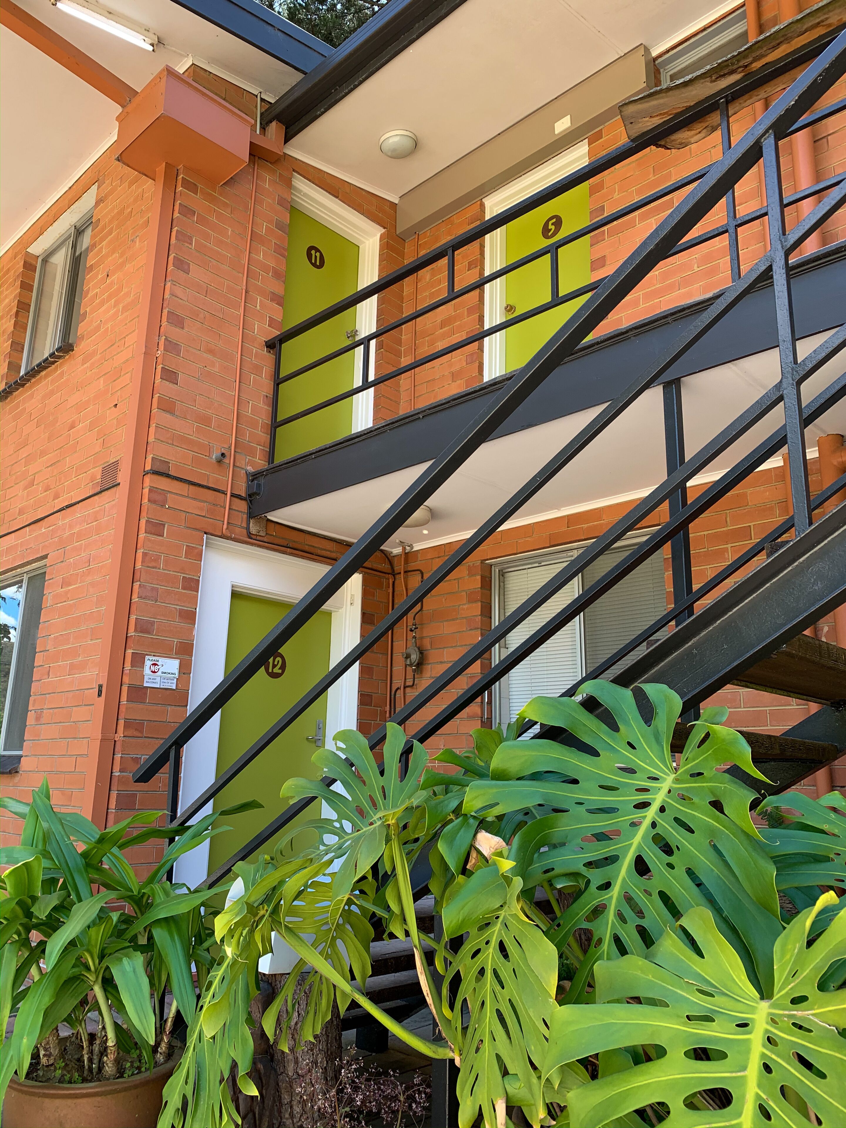A brick building with a black metal staircase, green doors, and potted plants.