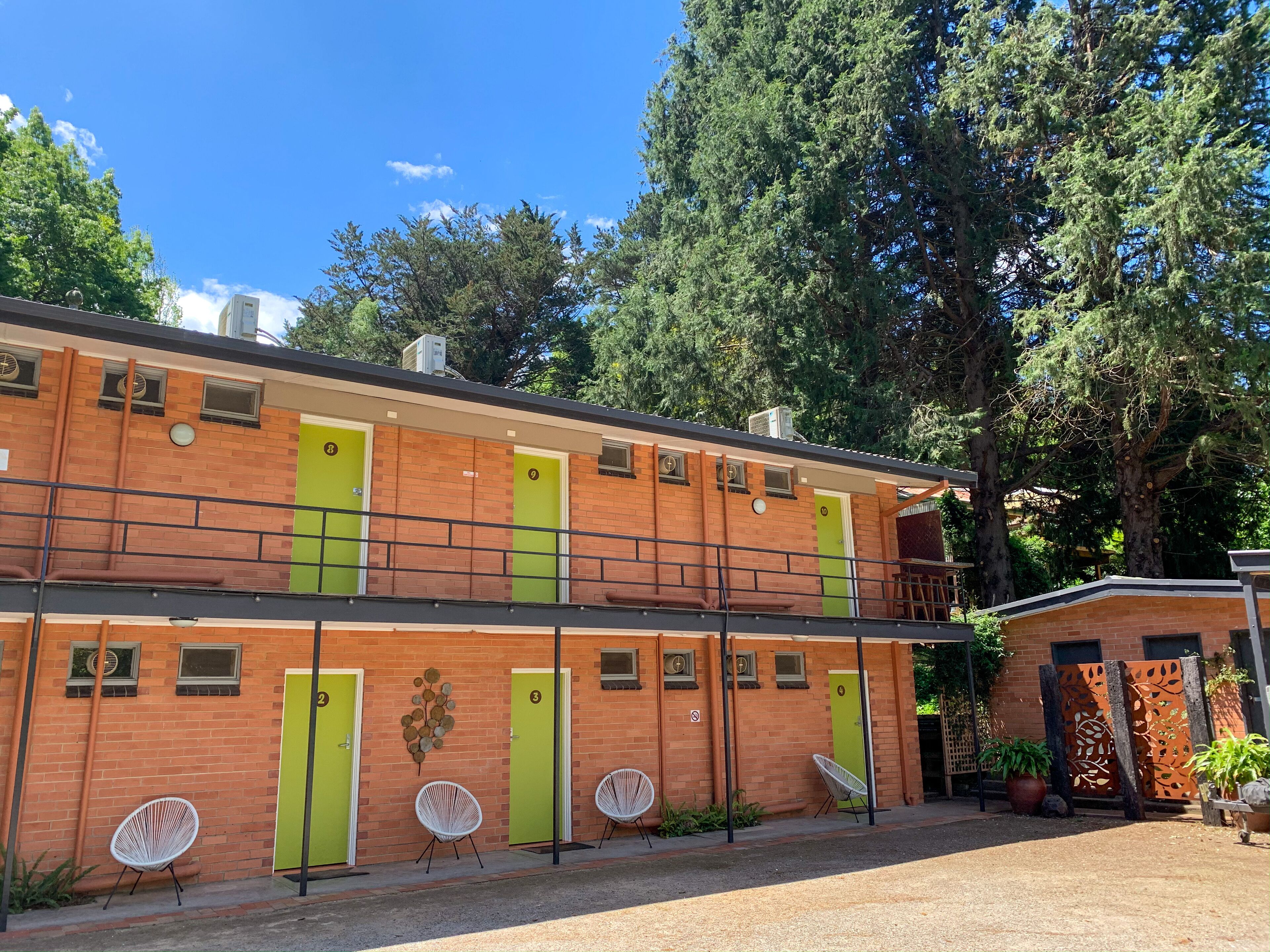 Un edificio de dos pisos con puertas verdes, un balcón y mesas al aire libre.