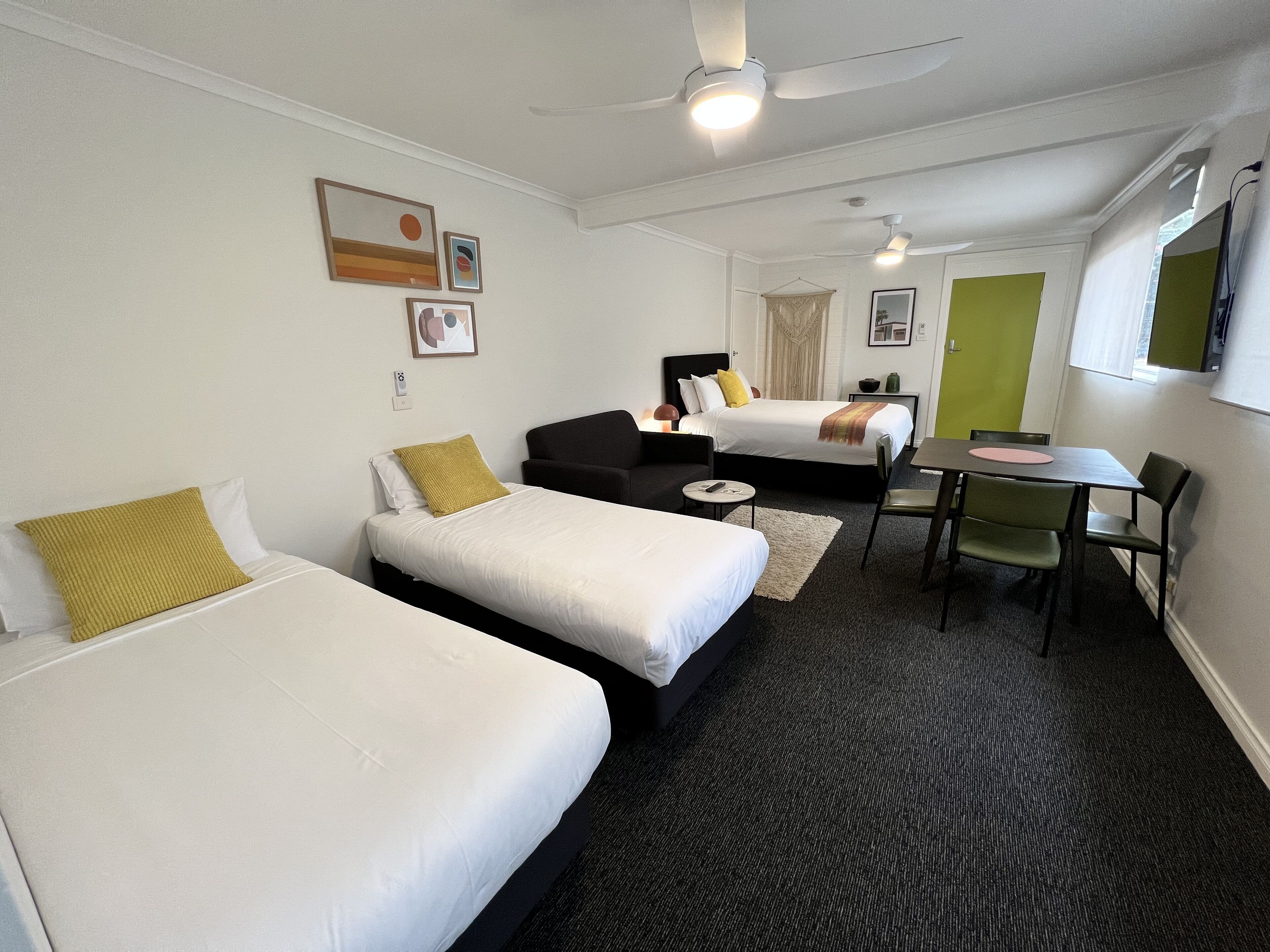 Une chambre d’hôtel avec deux lits, un bureau et une chaise. Elle est équipée de ventilateurs de plafond et possède une fenêtre.