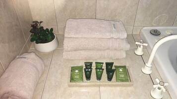 A bathroom with a bathtub, a potted plant, a stack of towels, and a tray of facial bar products.