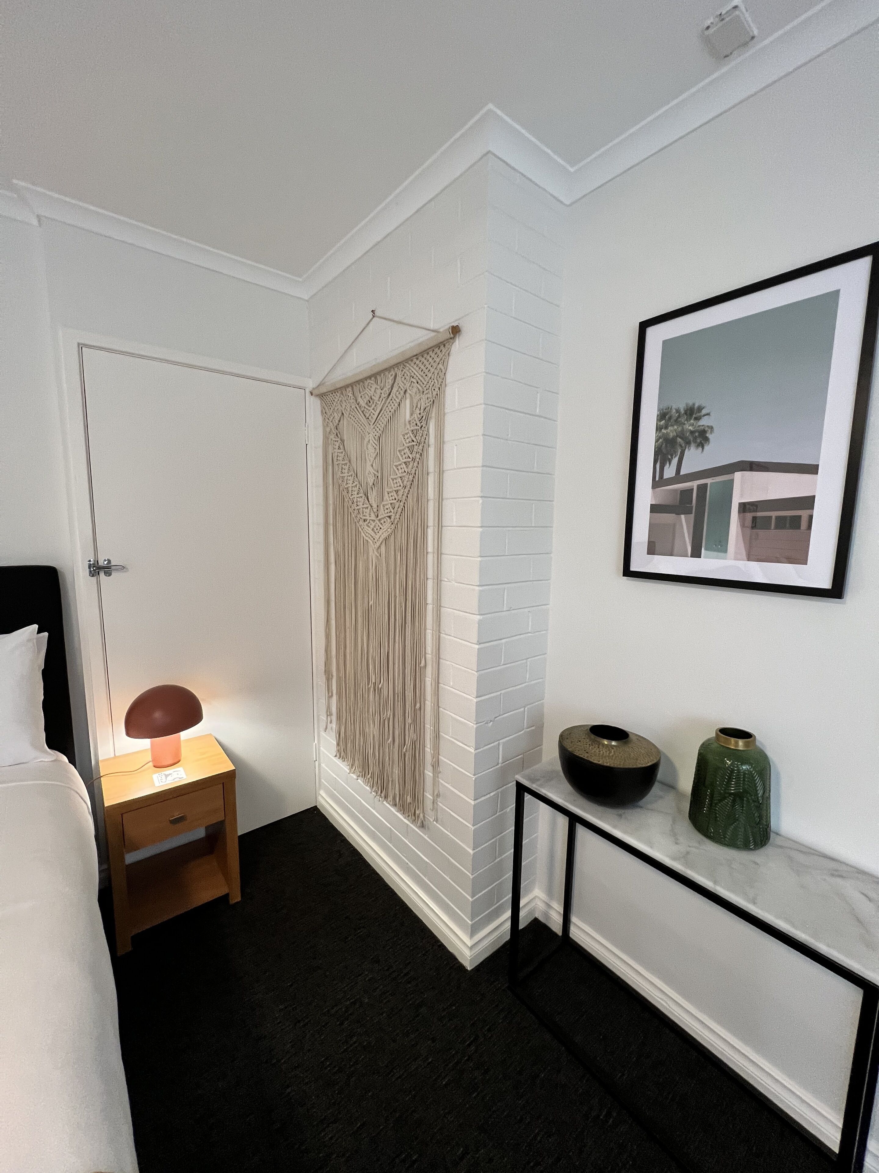 Ein Hotelzimmer mit einem Bett, einem Nachttisch mit Lampe, einem Wandbild und einem kleinen Konsolentisch mit Dekoration.