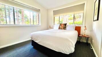 A modern hotel room with a large bed, two bedside tables, a nightstand, and a window with a view of trees.
