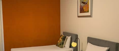 A hotel room with two single beds, a ceiling fan, a framed artwork on the wall, and a carpeted floor.