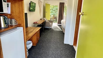 A compact hotel room with a kitchenette, a bed, a small table, and a view of the outdoors.