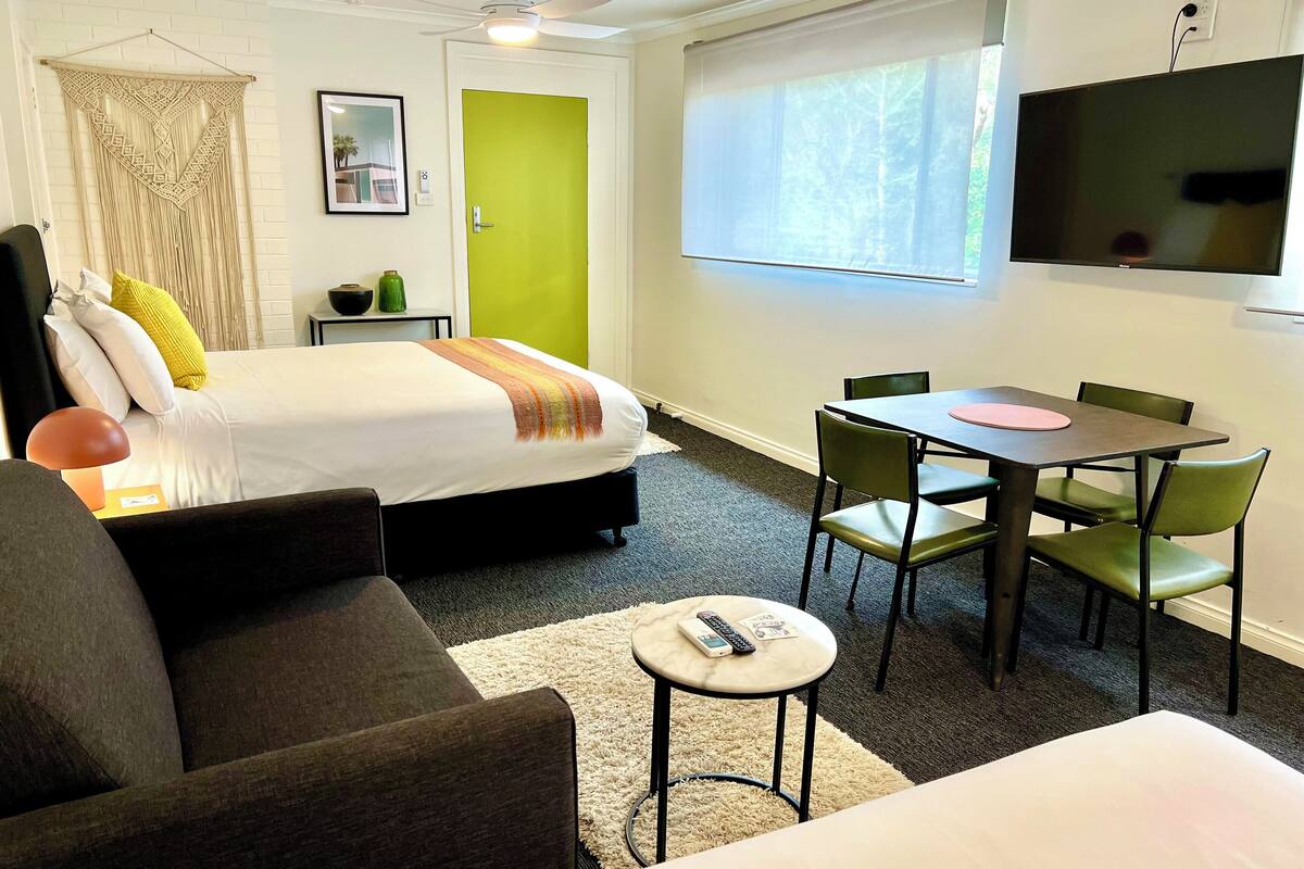 Une chambre d’hôtel avec un lit, un bureau, une chaise, un canapé, une télévision et une fenêtre.