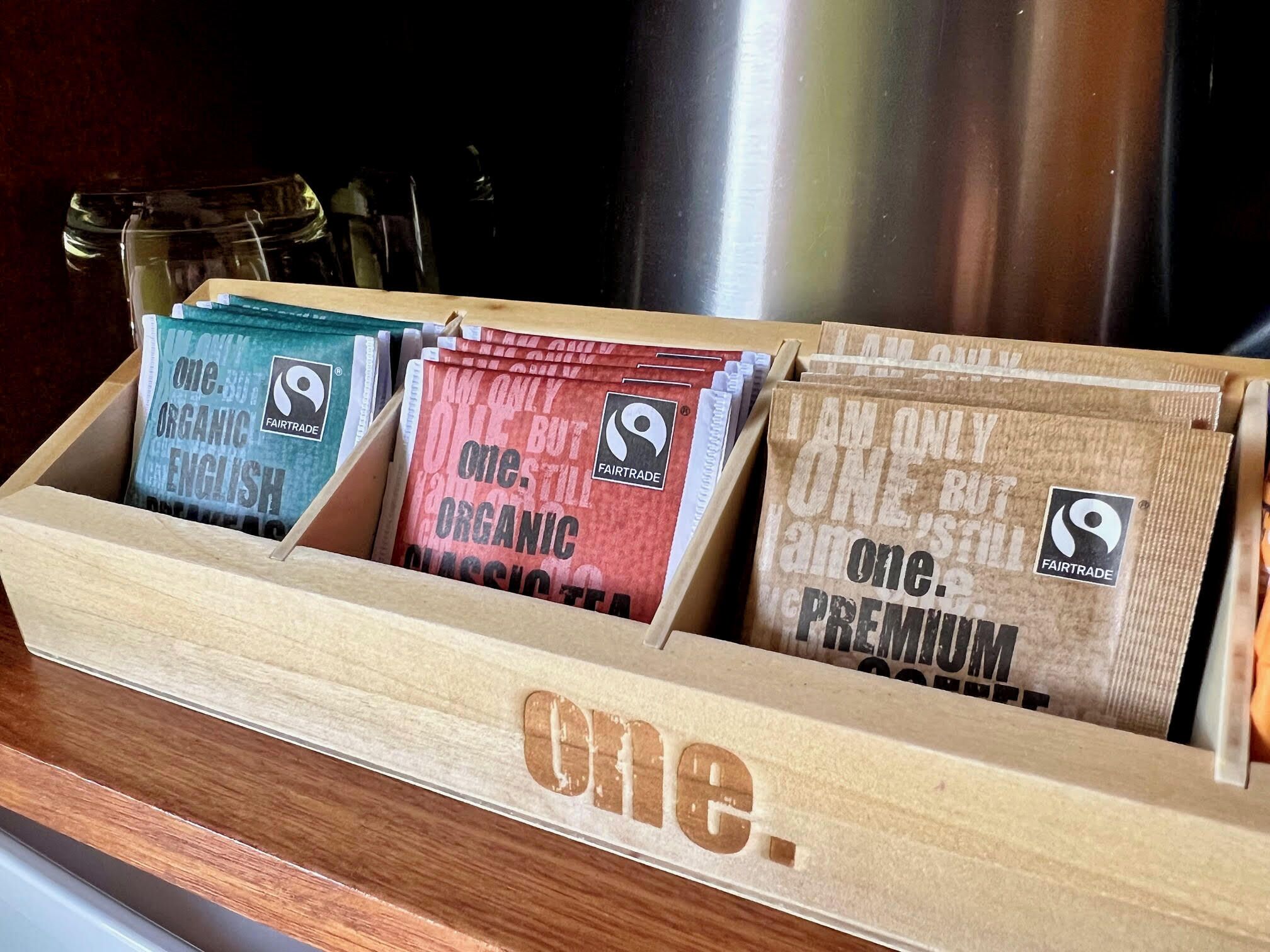 A wooden box with compartments containing tea bags labeled "one. organic" and "one. but still premium."