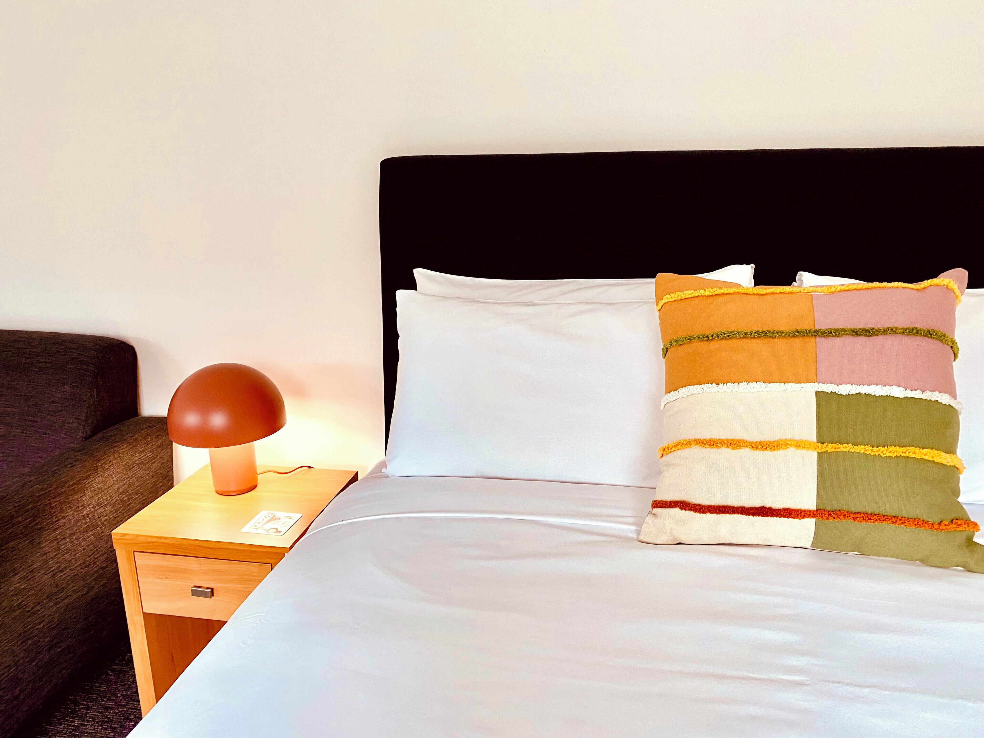A neatly made bed with a white pillow and a colorful striped blanket.