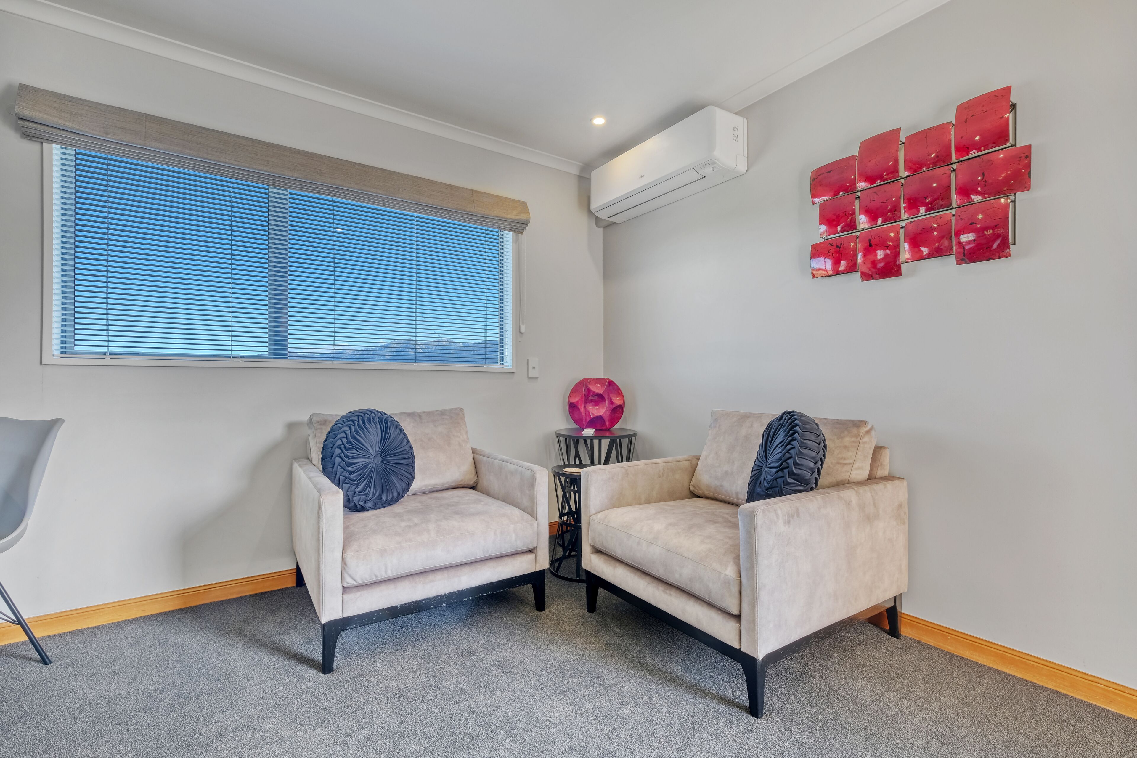 A room with two beige armchairs, a small round table, a decorative pink sphere, and a window with blinds.