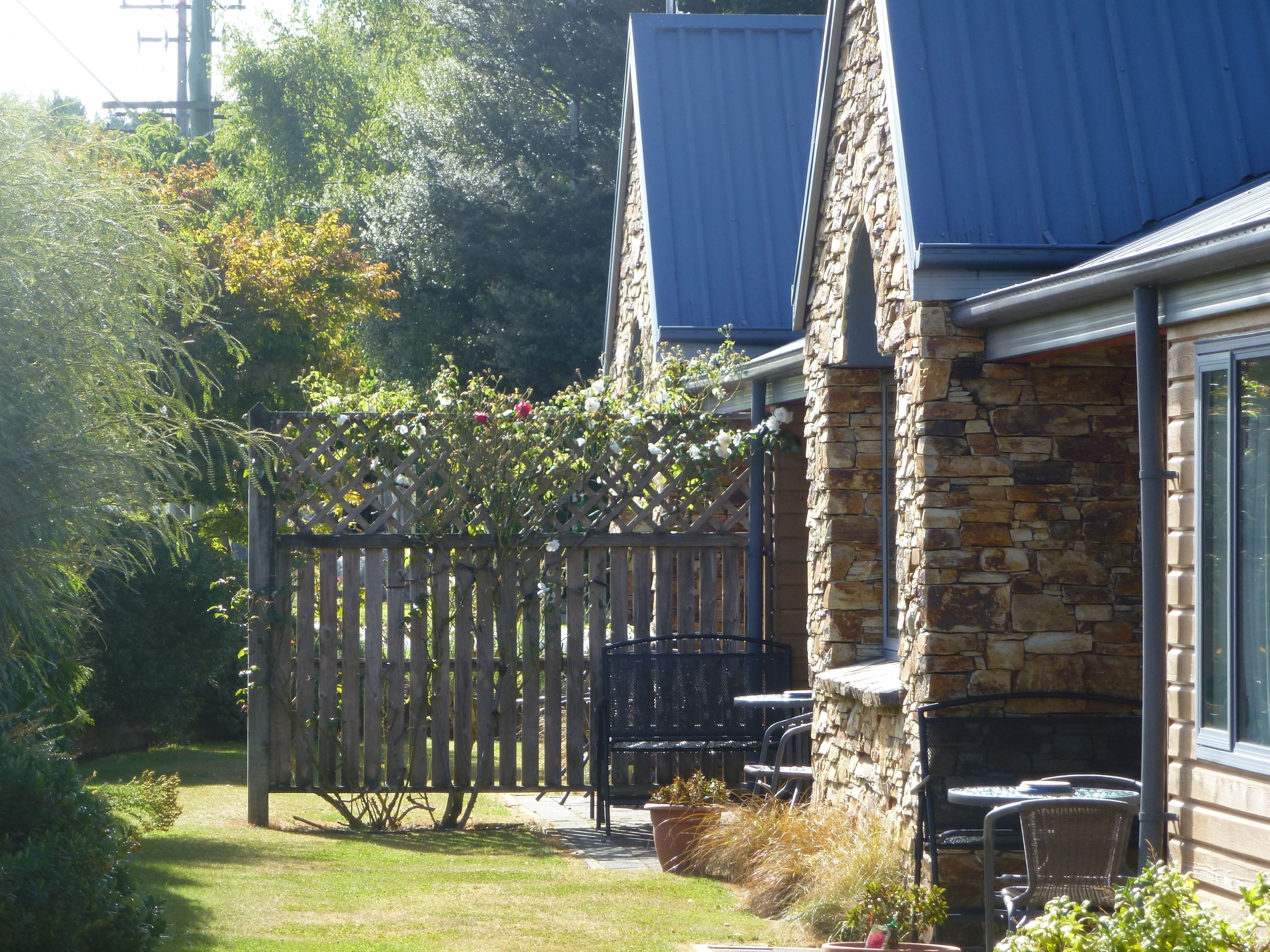 A stone building with a blue roof, a wooden fence, and outdoor seating.