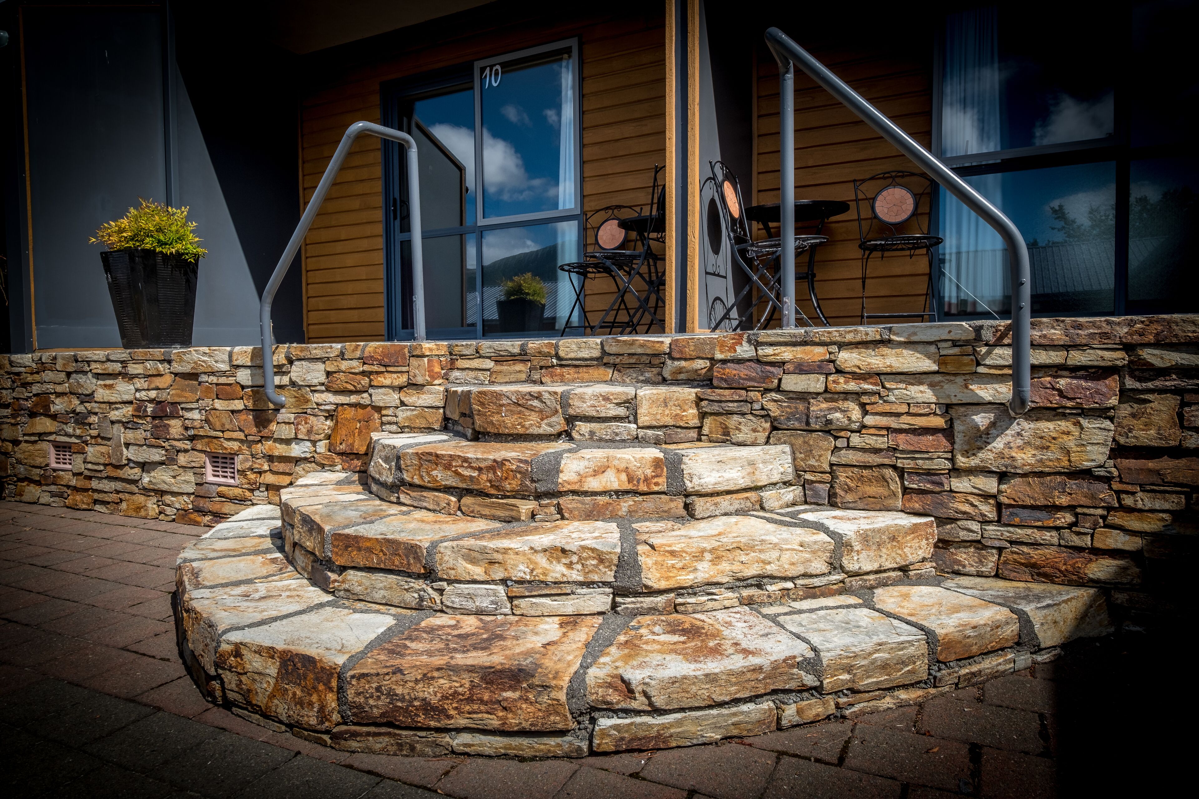 A stone staircase leading to a wooden door, with outdoor seating and a potted plant visible.