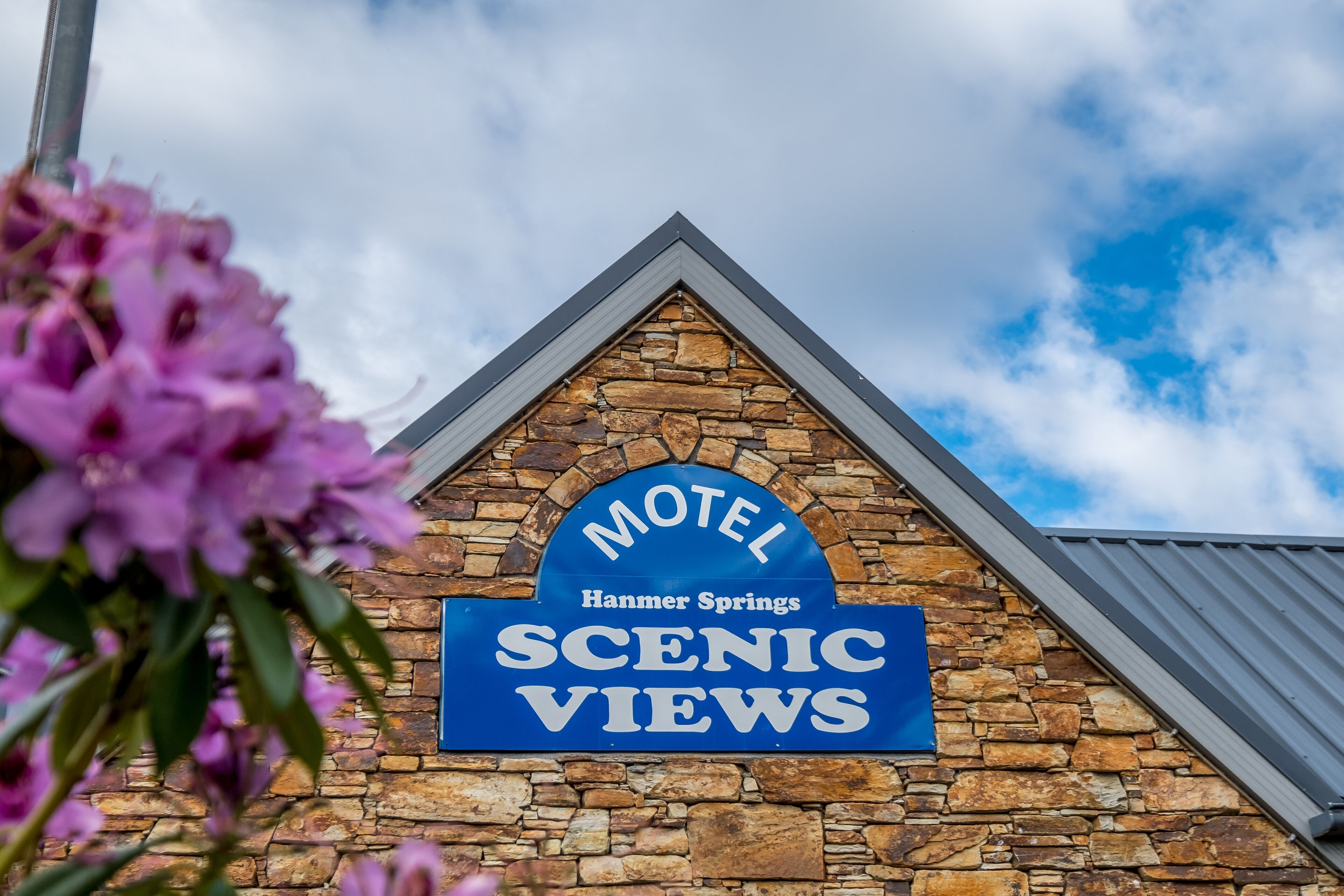 A motel sign with the text "Motel Hammer Springs Scenic Views" against a stone wall.