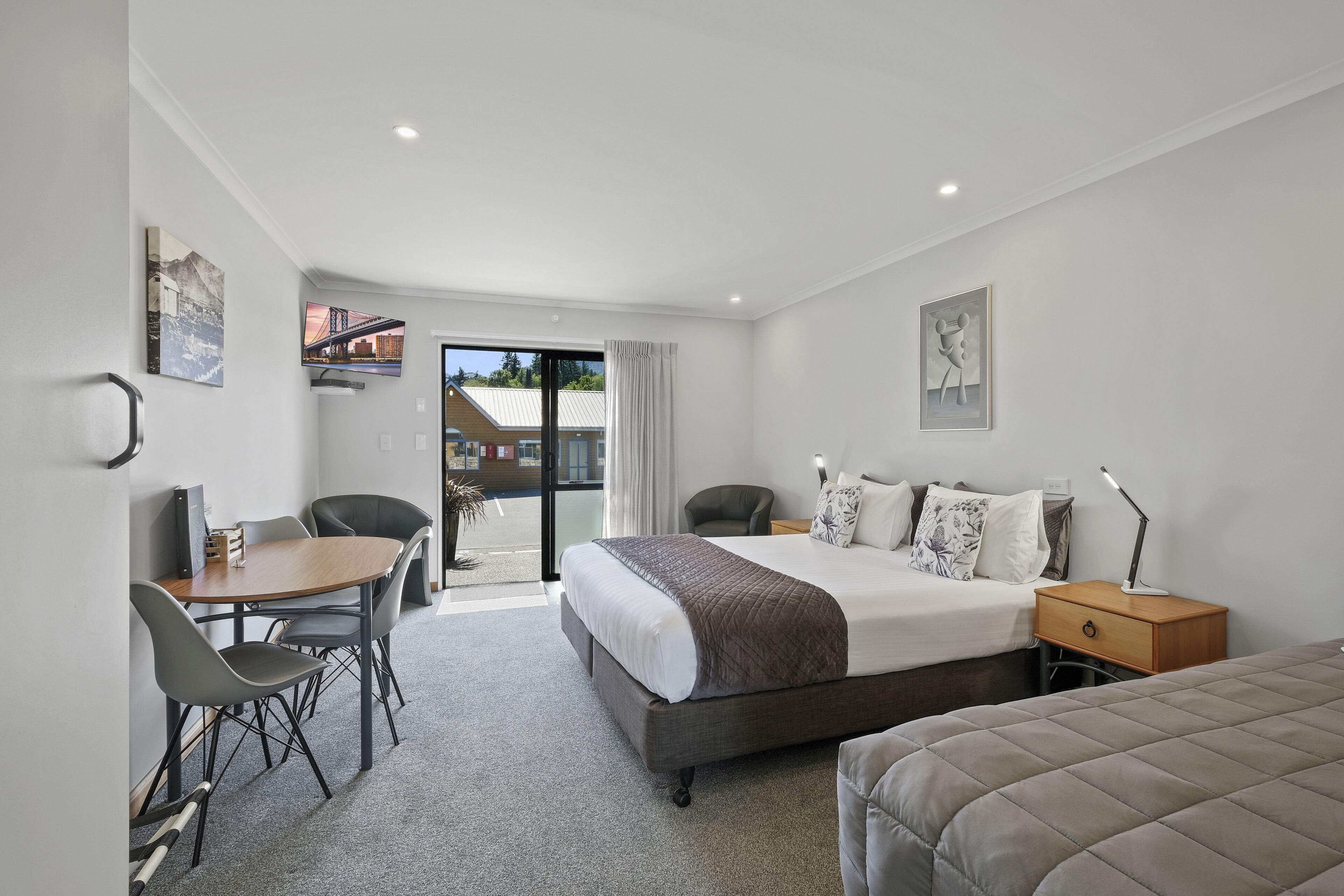 A modern hotel room with a bed, desk, chairs, and a view of the outside.