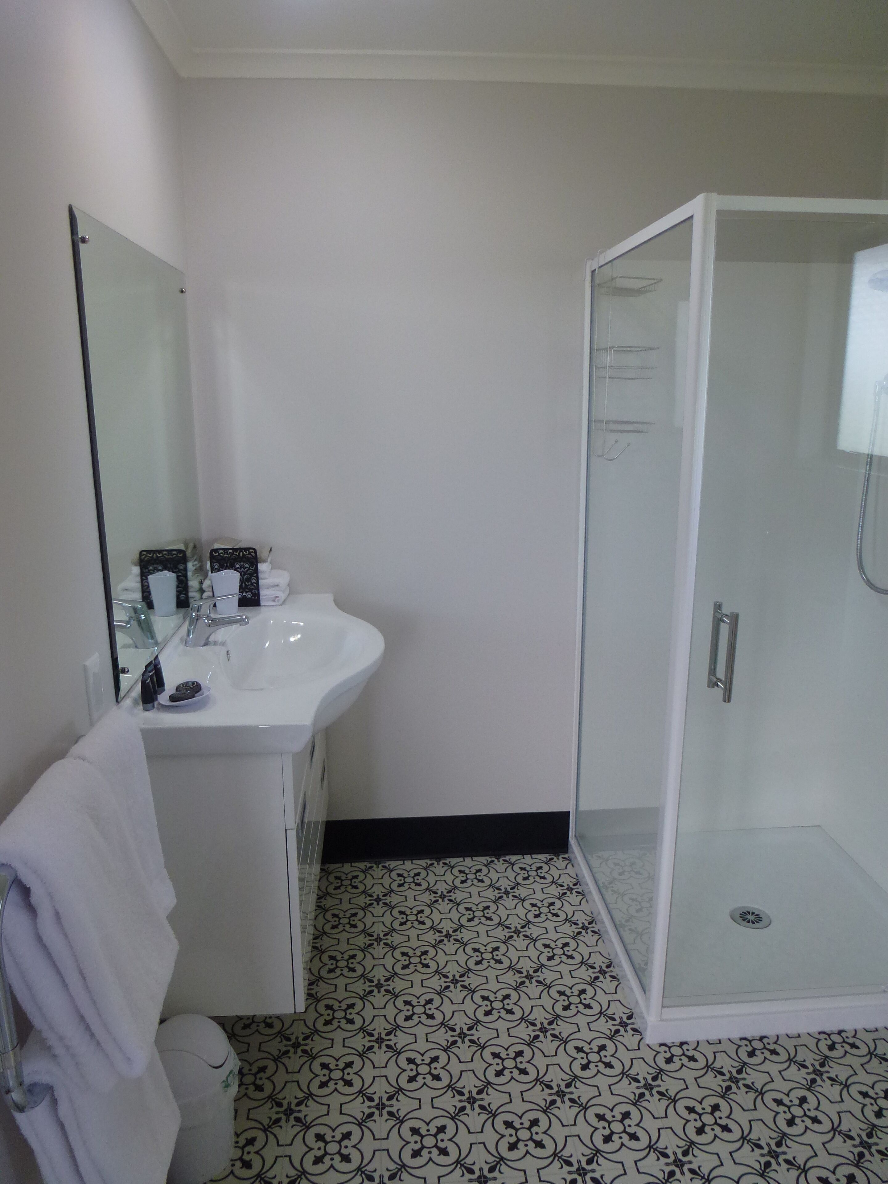Un baño con un lavamanos blanco, cabina de ducha con mampara de cristal y baldosas de suelo con estampado.