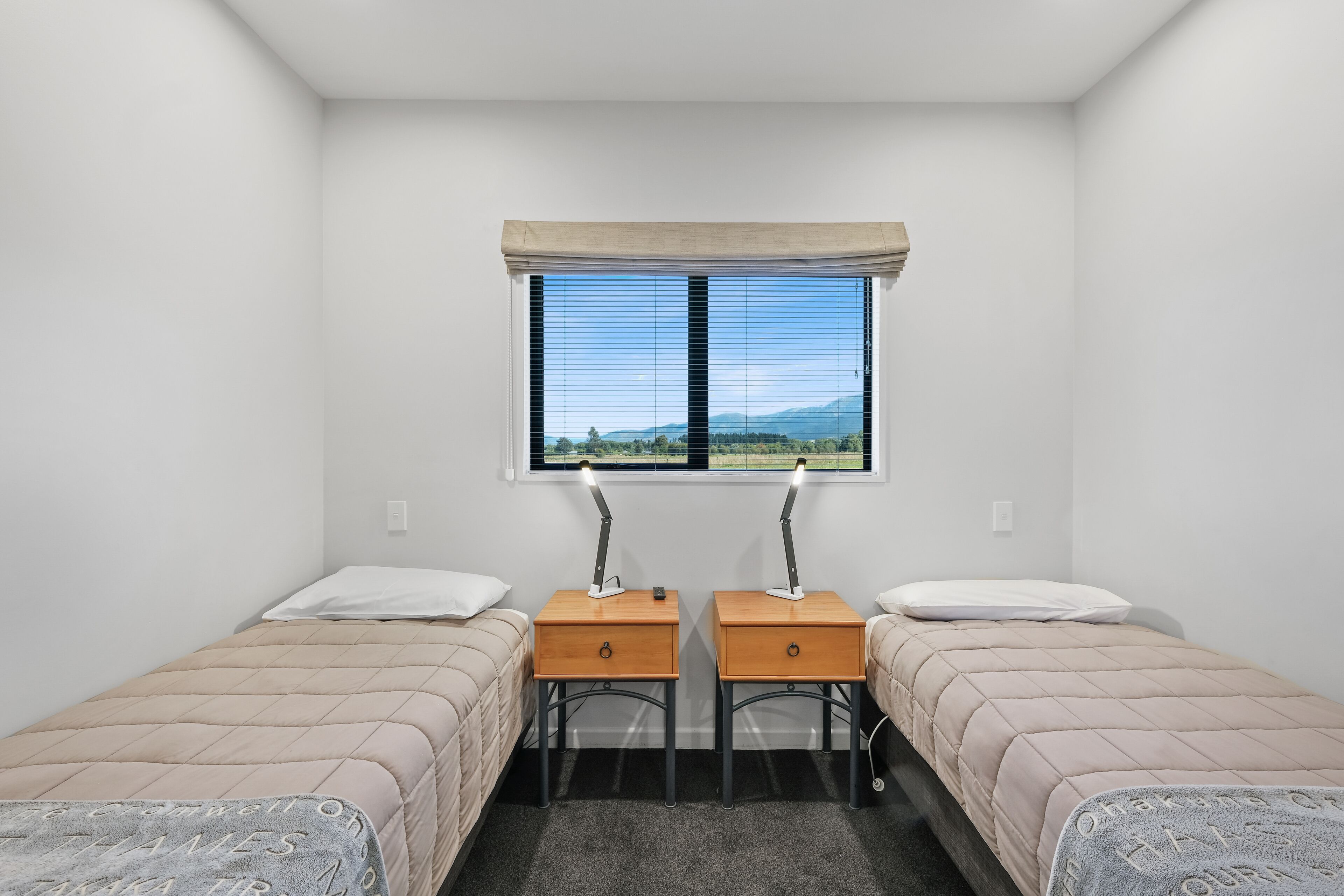 Una habitación con dos camas, una ventana con persianas y un escritorio con lámpara.