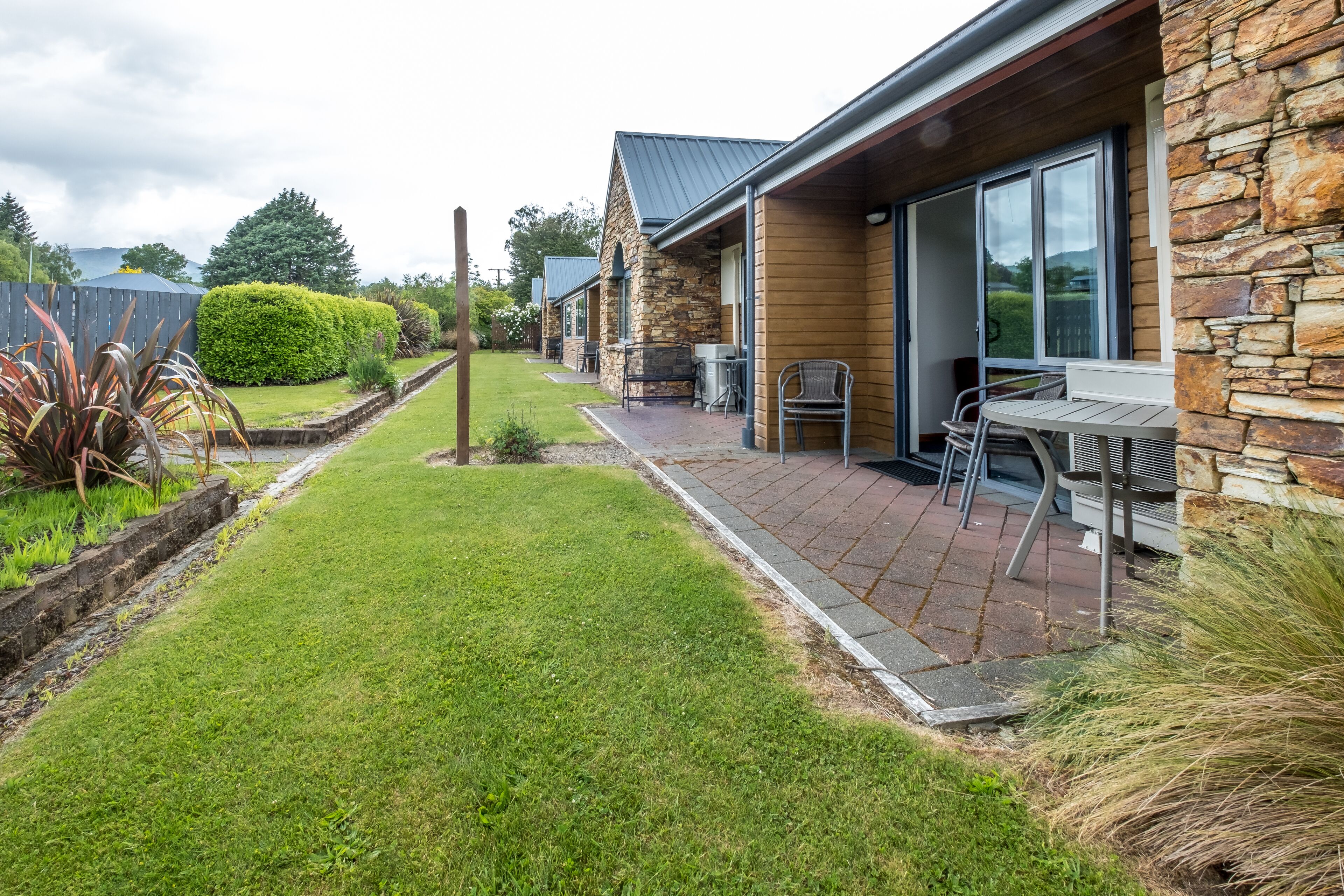 A house with a stone exterior, a paved patio with outdoor furniture, and a well-maintained lawn.