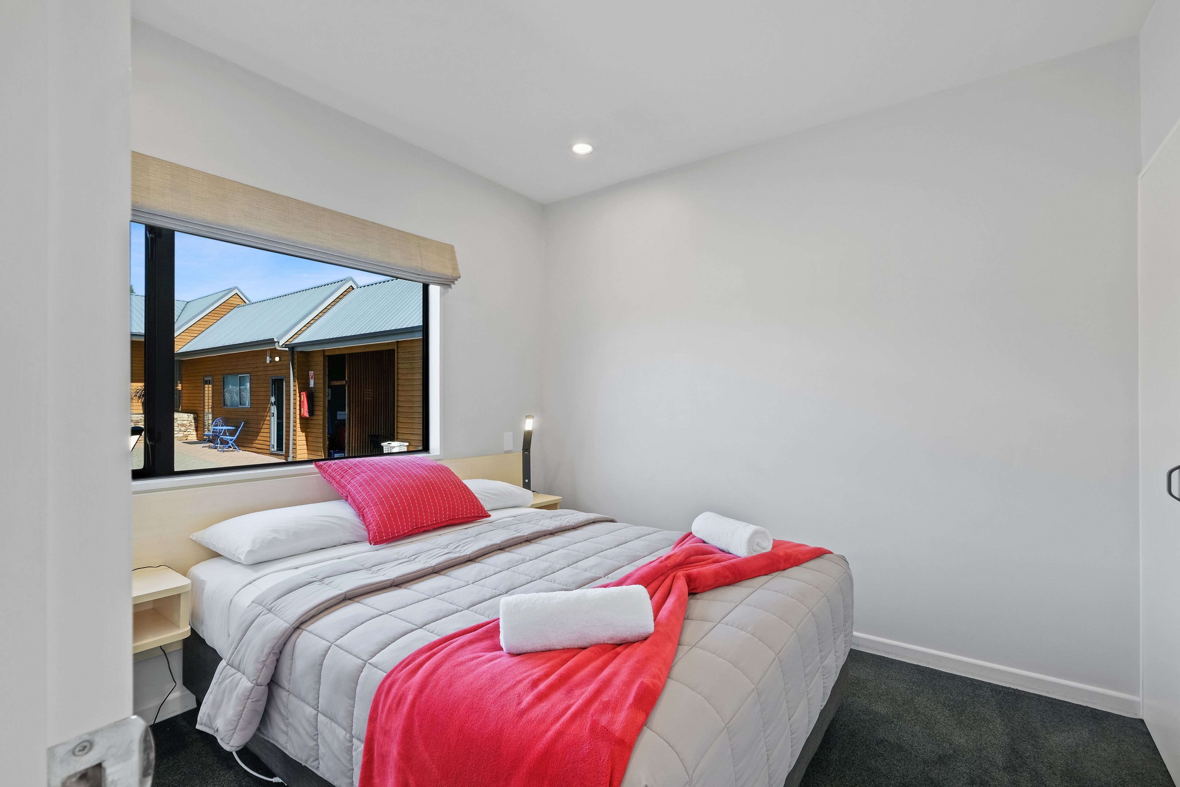 Une chambre d’hôtel moderne, dotée d’un grand lit, d’une fenêtre donnant sur la façade de l’immeuble et d’une table de chevet.