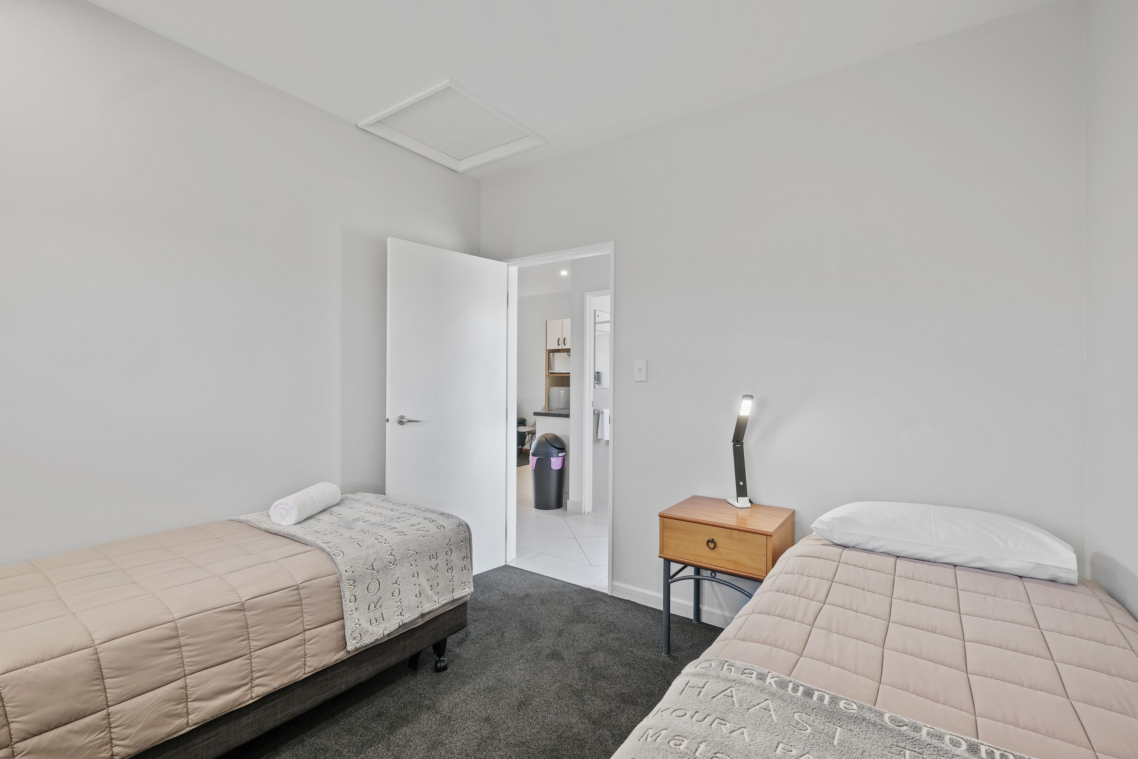 A bedroom with two beds, a nightstand, and a door leading to a bathroom.
