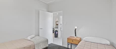 A bedroom with two beds, a nightstand, and a door leading to a bathroom.