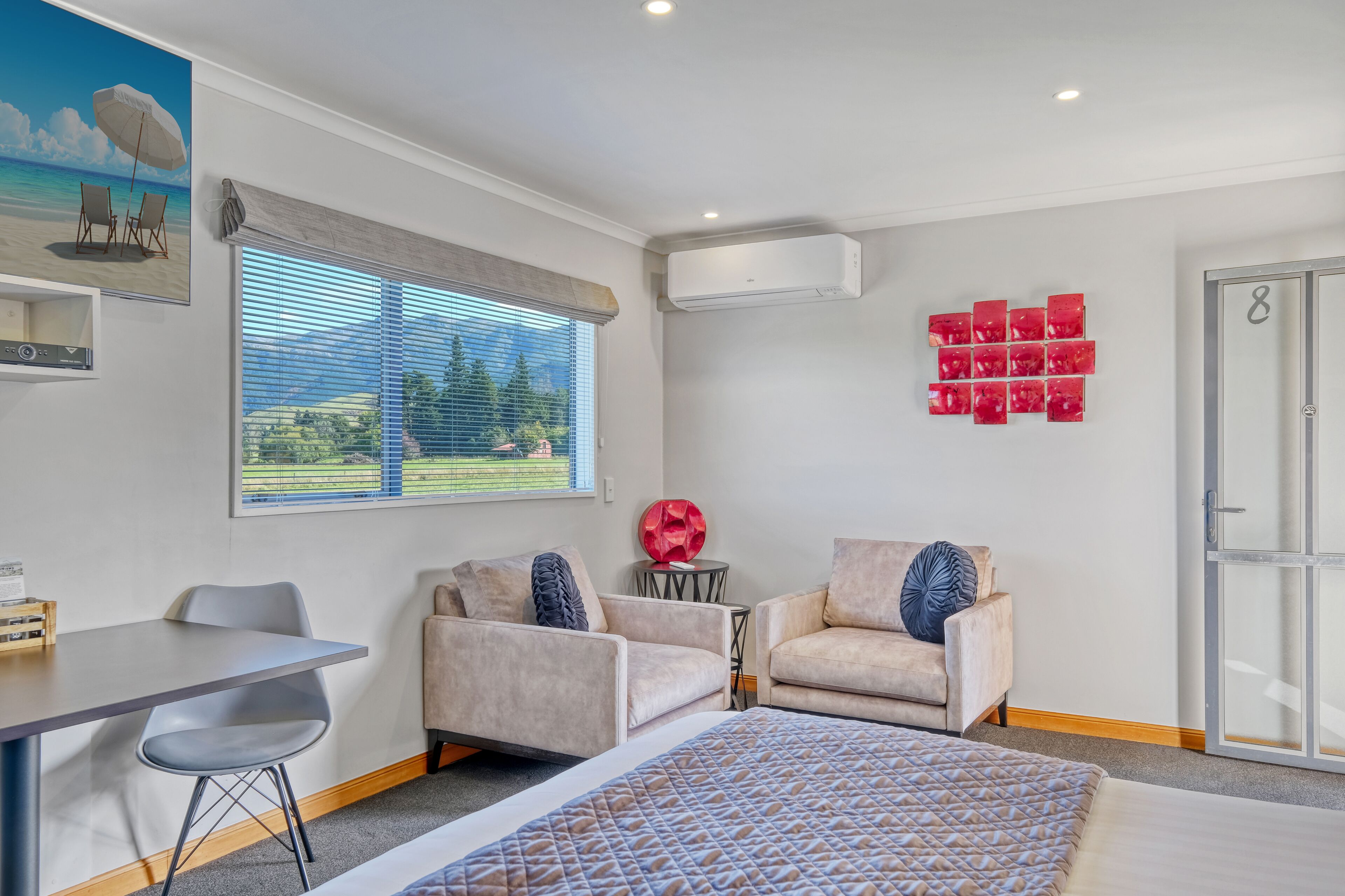 A modern room with a bed, two armchairs, a small table, and a window with blinds.