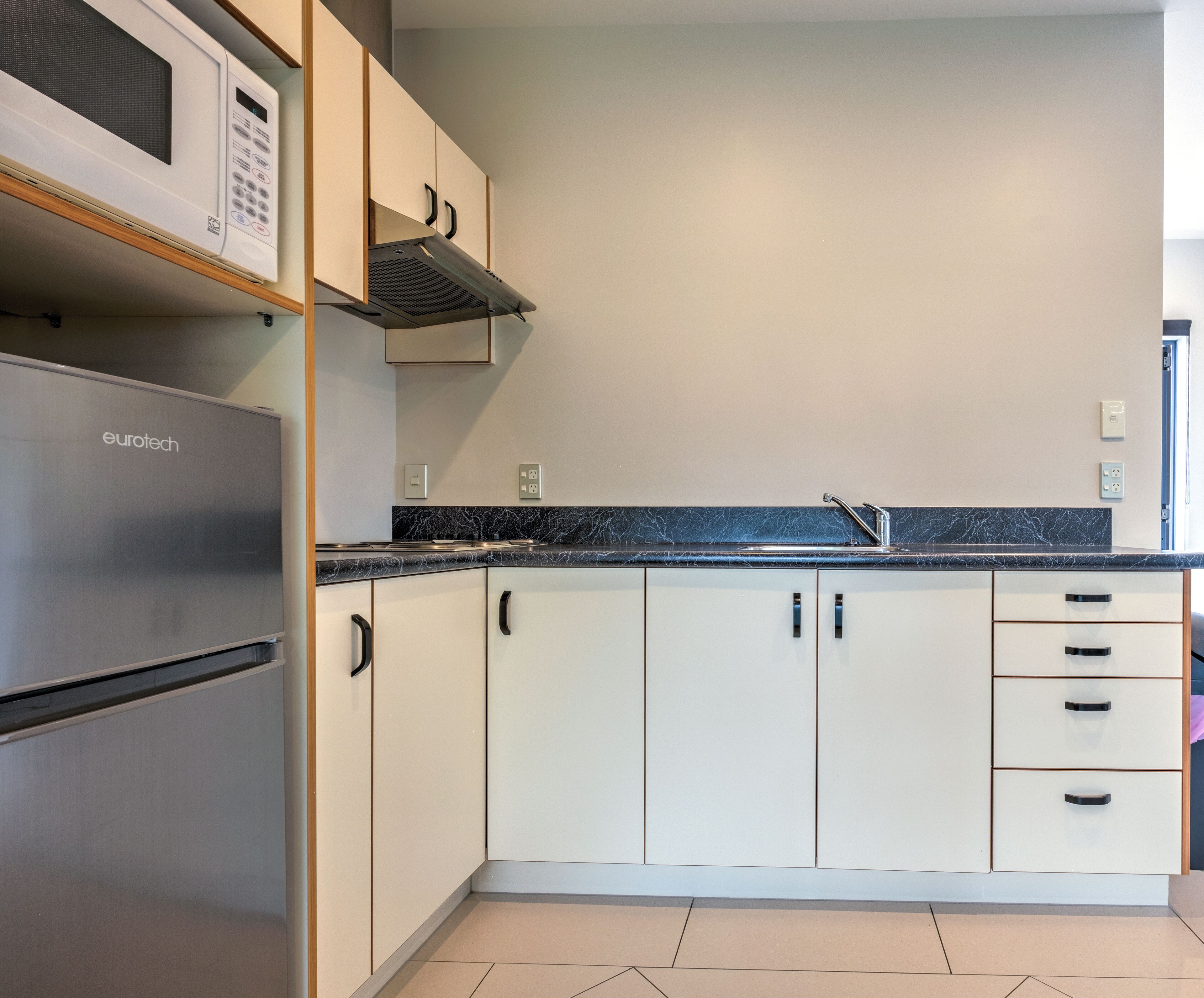 A kitchen with white cabinets, a stainless steel refrigerator, a microwave, and a black countertop.