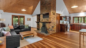 A spacious living room with a fireplace, wooden flooring, and a high ceiling. - Hunchy Hideaway (Hunchy)