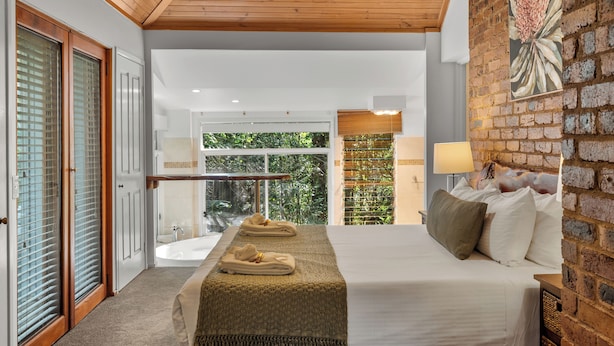 A modern hotel room with a large bed, a view of greenery, a wooden ceiling, and a brick wall. - Hunchy Hideaway (Hunchy)