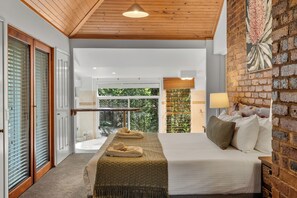 Una habitación de hotel moderna con una cama grande, vistas a zonas verdes, techo de madera y pared de ladrillo.