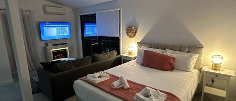 A hotel room with a bed, a sofa, a TV, and a fireplace.