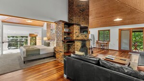 A modern living room with a brick fireplace, wooden flooring, a black leather sofa, and a dining area with a table and chairs. - Hunchy Hideaway (Hunchy)