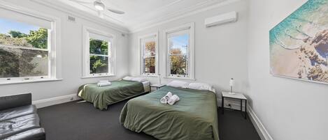 A room with two beds, a ceiling fan, and large windows.