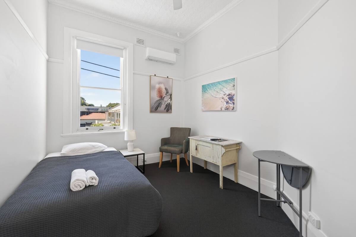 A hotel room with a bed, a desk, a chair, a small table, and artwork on the walls.