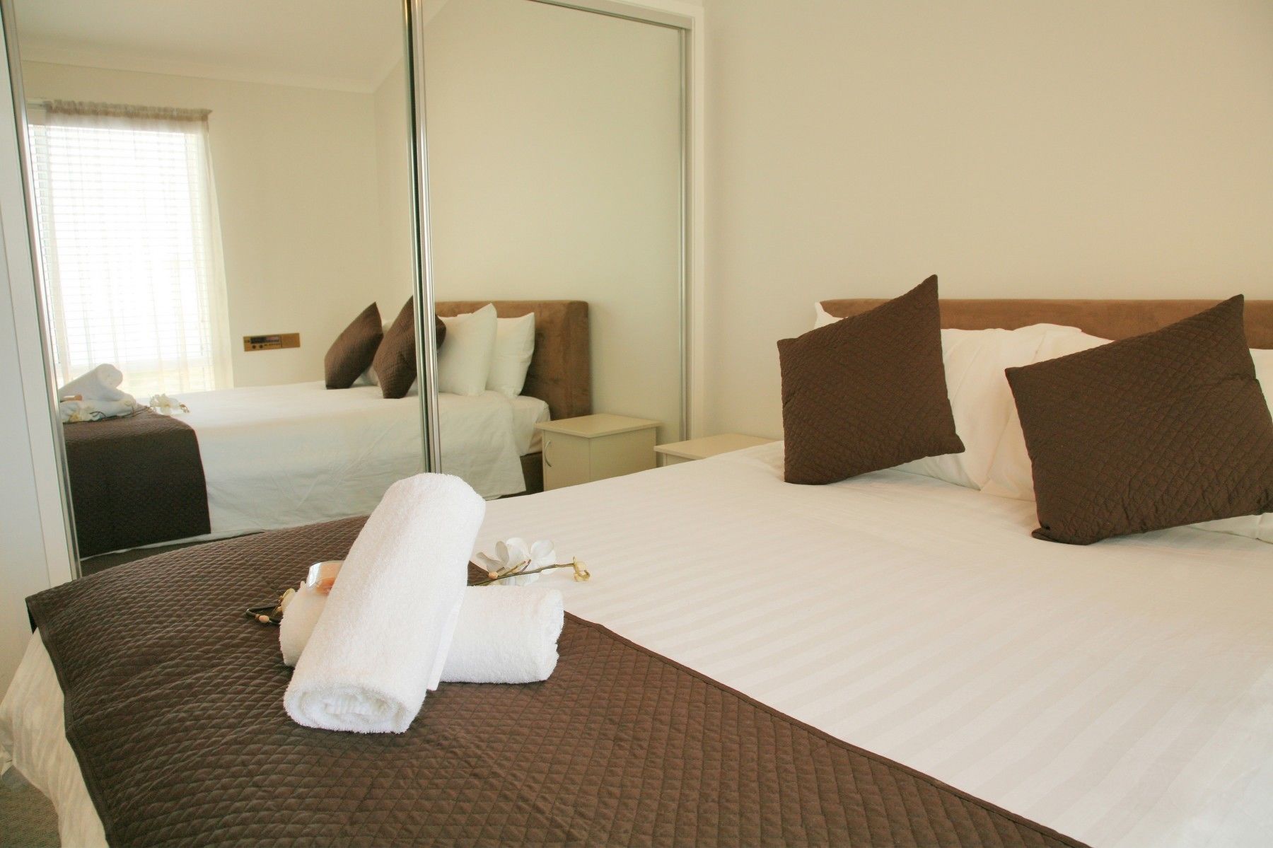 A hotel room with a large bed, a bedside table, a mirror, and a window with blinds.