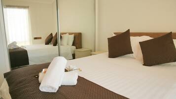 A hotel room with a large bed, a bedside table, a mirror, and a window with blinds.