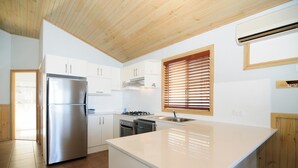 A modern kitchen with white cabinets, a stainless steel refrigerator, a built-in oven, and a large island with a sink. - Surf Beach Holiday Park (Kiama)