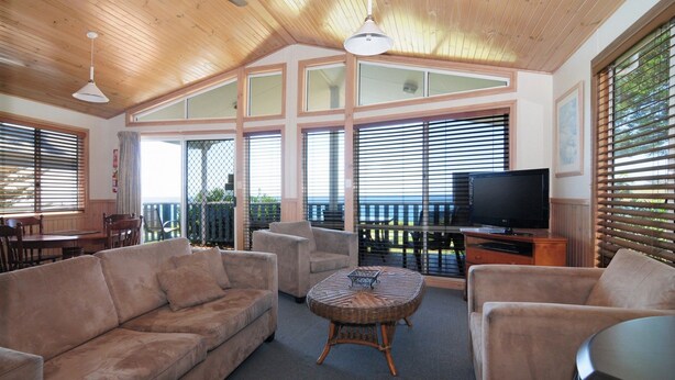 A spacious living room with a high ceiling, large windows, and a balcony. - Surf Beach Holiday Park (Kiama)