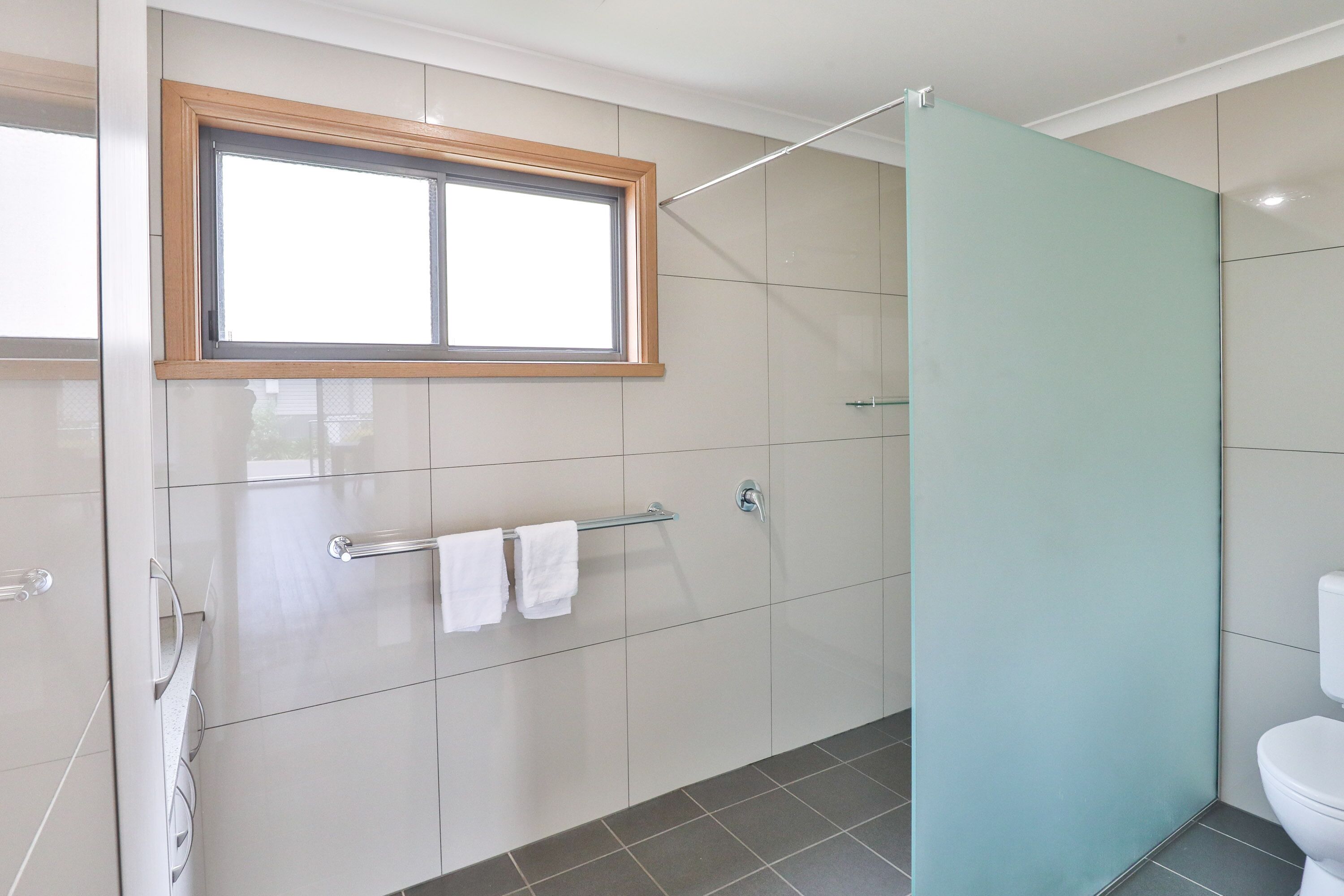 Un baño moderno con cabina de ducha de vidrio, un inodoro y un perchero con dos toallas.