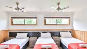A hotel room with three single beds, wooden headboards, a marble accent wall, and two windows with blinds.