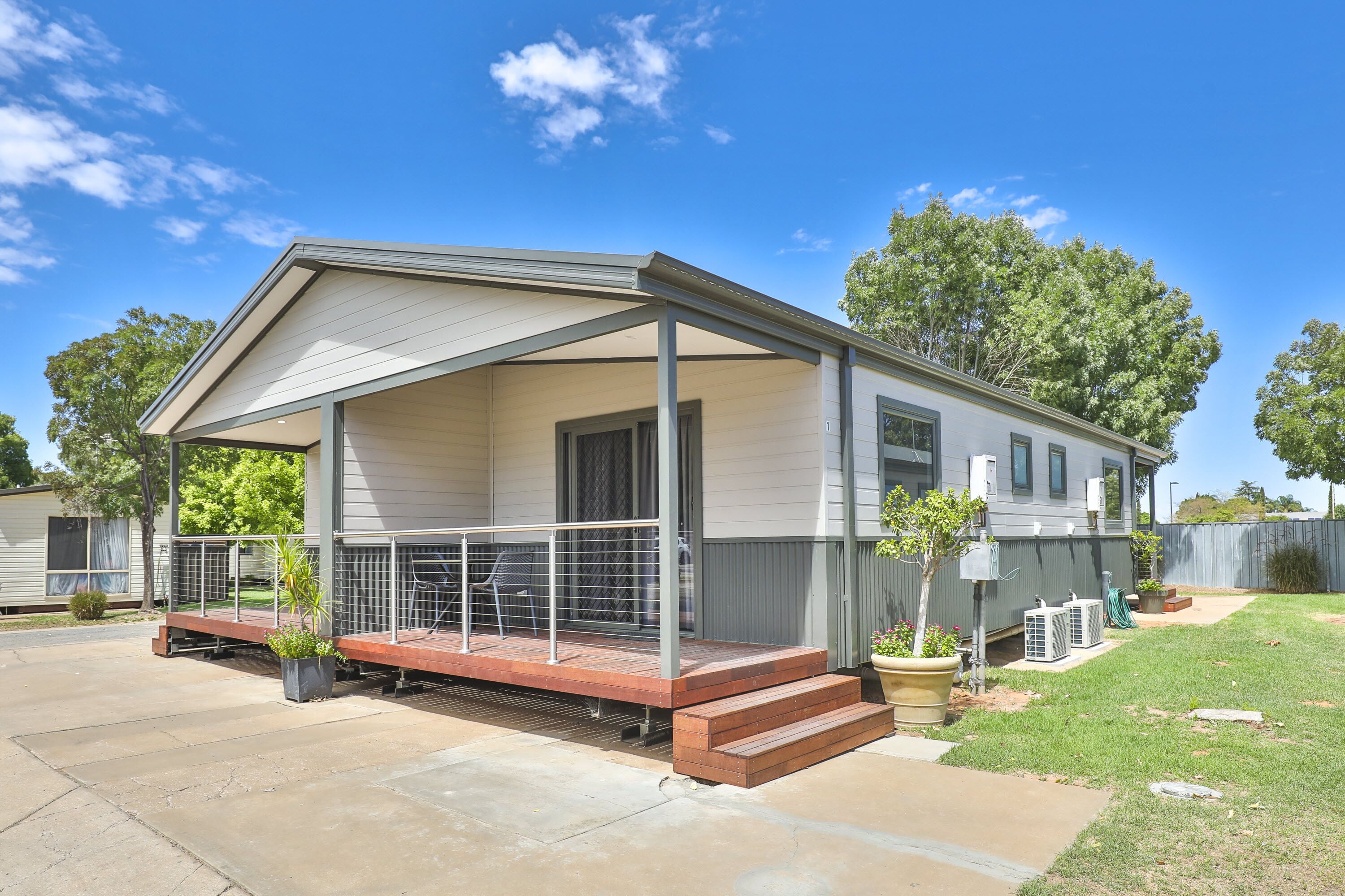 A single-story mobile home with a covered porch, a small front yard, and a clear blue sky.