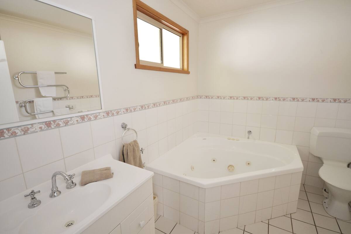 A bathroom with a large bathtub, a separate sink, a toilet, and a window above the sink.