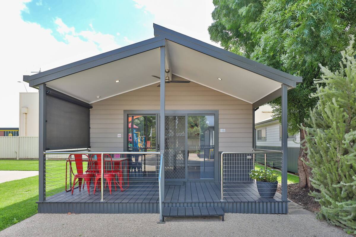 A covered outdoor area with a table and chairs, a small garden, and a pathway leading to a building.