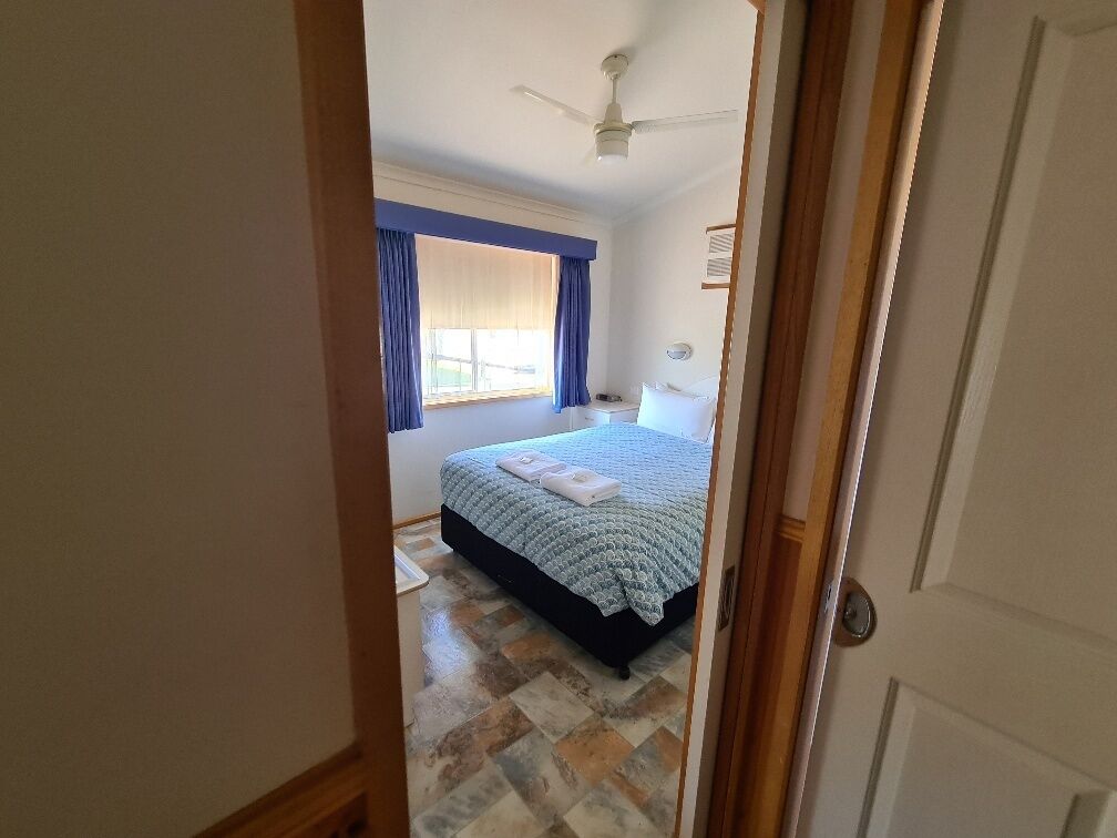 A bedroom with a bed, a ceiling fan, a window with curtains, and a tiled floor.